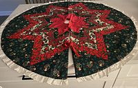 Quilted Christmas tree skirt laid flat showing full star patterned patchwork, green base with Christmas motifs, and cream ruffled edge.
