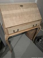 Front view of the refinished vintage solid maple secretary desk showing the light wood finish and original brass hardware on the closed drop front panel and drawer.