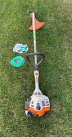 Stihl gas grass trimmer laid on grass with two green trimmer line spools