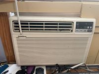 Front view of beige GoldStar window air conditioner unit installed in a window, showing vent and control panel with buttons.