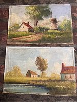 Two antique oil paintings placed on a textured fabric surface. Visible rural Dutch landscape scenes with cottages, a windmill, and trees. Both signed DeGryss.