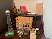 Overview of the lot showing various barware and collectibles including bottles, boxes, and decorative items arranged on a wooden surface
