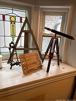 Photo showing all lot items placed on a windowsill including metal frame, wooden stands, and decorative telescope on tripod.
