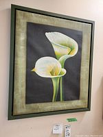 Full view of framed calla lily painting hung on wall showing two white flowers with green border and black background.