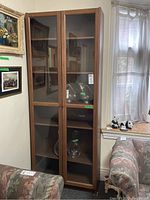 Full view of IKEA wood finish cabinet with glass doors and five shelves inside, showing fit within a room.