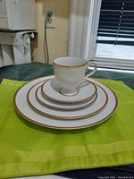 Stack showing the set of plates of various sizes and a teacup with handle and gold rim on top.