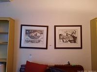 Two framed black and white prints hanging side by side on a wall above a seating area. Both prints are numbered and signed, one is 3/36.