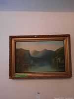 Framed landscape painting showing lake and mountains with sailboat, decorative gold frame with crack damage