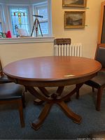 Full view of round cherry pedestal table with chairs and window background