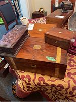 Four wooden boxes of varying sizes laid on a patterned tablecloth, showing tops and sides including brass details and engraved plates