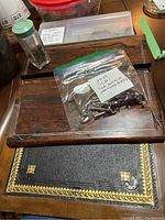 Old keys in a clear plastic bag labeled 'Keys Old! For Antique Writing Boxes' on top of dark polished wooden boards and a leather writing surface with gold detailing.