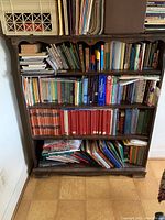 Front view of wooden bookcase filled with various books, showing overall shape, shelving and condition.
