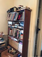 Side angle view of tall wooden bookshelf filled with books, showing the height and shelves fully loaded, highlighting condition and wear.