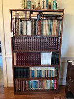 Front view of tall wooden bookshelf filled with various hardcover books on five shelves.