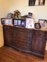 Front view of Bernhardt wooden buffet cabinet with multiple framed photos on top.