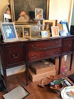 Front view of vintage wooden buffet table with framed photos on top and storage boxes below.