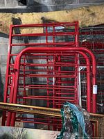Photo showing red metal bunk bed frames with rounded corners and tubular design stacked vertically on concrete floor with insulation in background.