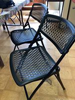 Two black plastic folding chairs with ventilated plastic seat and back, metal frame, positioned side by side indoors.