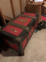 Side view of large red and black Asian themed chest with metal reinforcements on corners and relief images of traditional figures on panels.