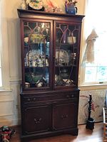 Front angled view of vintage china cabinet showing glass display doors with china inside, drawers, and lower cupboards.