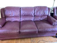 Full front view of the burgundy leather couch showing three seats and cushioned backrests.
