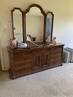 Full view of wooden dresser with three-pane mirror attached. Some items placed on dresser are not included.