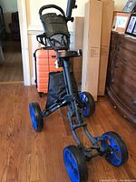 Angle view of Caddytek golf cart showing handle with controls, blue wheels, and attached storage bag.