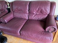 Front view of burgundy leather loveseat showing two seat cushions and rolled armrests with nailhead trim