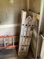 Krause multi-positional ladder folded and standing upright in storage corner with hinge mechanisms visible.