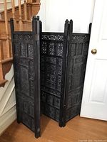 Three-panel wooden folding screen positioned near staircase and wall, showing front view and detailing of carved panels.