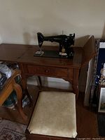 Full view of Singer sewing machine on wooden table with bench seat in front