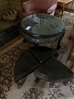 Round dark wooden table with ornate Asian themed carved wood under glass top, placed on patterned carpet