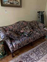 Upholstered floral-patterned 3-seater couch with multiple matching pillows positioned in a room with a rug and decorative items