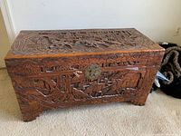 Front view of the carved wooden chest showing detailed Asian-themed figurative carvings and decorative border.