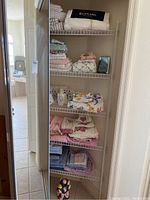 Photo showing mixed bathroom linens folded on wire shelf, including Ralph Lauren towels, pastel and floral towels, and washcloths.