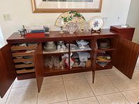 Sideboard open showing china, crystal glassware, serving trays and cloth items inside