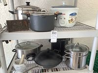 Two plastic shelves with various kitchen appliances and cookware items including pots, a rice cooker, slow cooker, steamer pot, bacon press, and mortar and pestle.