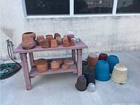 Flower pots and plates displayed on a wooden table and concrete floor, various colors and materials visible including terracotta and plastic.
