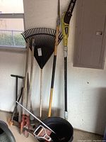View showing plastic leaf rake, Ryobi electric pole saw, wooden handled shovel and gardening hoe, metal gardening bucket.
