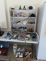 Wide view of table and metal shelf displaying assorted hardware including funnels, hose nozzles, small containers, and tools