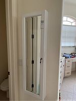 Front view of the closed white jewelry cabinet mounted on a wall, showing the full-length mirror door.
