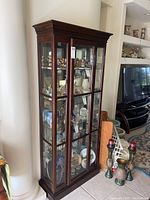 Front and side view of the tall wooden curio cabinet with glass doors and shelves, displaying various decorative items inside.