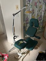 Full view of green padded adjustable massage chair with infrared heat lamp on casters in the background.