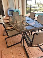 Full view of rectangular glass top patio table with six matching chairs around it on a brick patio.