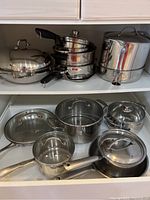 Overview of all pots and pans stored in shelves and drawer, showing variety and condition.