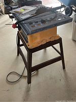 Yellow and black Pro Tech 10-inch bench saw on metal stand, showing corrosion on work surface and blade attached.