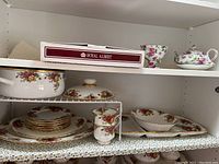 Two-shelf overview showing boxed platter, teacups, covered casserole on rack, round platter and stacked dessert plates