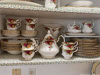 Full view of shelves showing cups, plates, teapot, sugar bowl, creamer and vase in Old Country Roses pattern