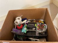 Overview of a cardboard box filled with sewing supplies including thread, pincushion, scissors, needles, and other items
