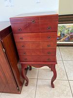 Front view of wood silverware armoire showing four drawers and metal handles on a tiled floor.